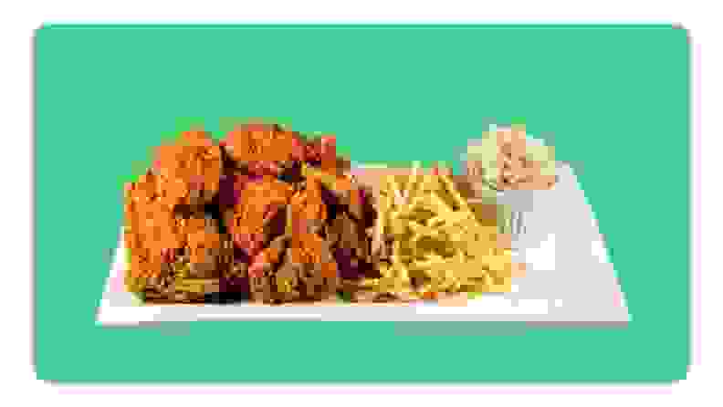 A platter of fried chicken, fries and a small cup of coleslaw on top of white plate in front of green background.