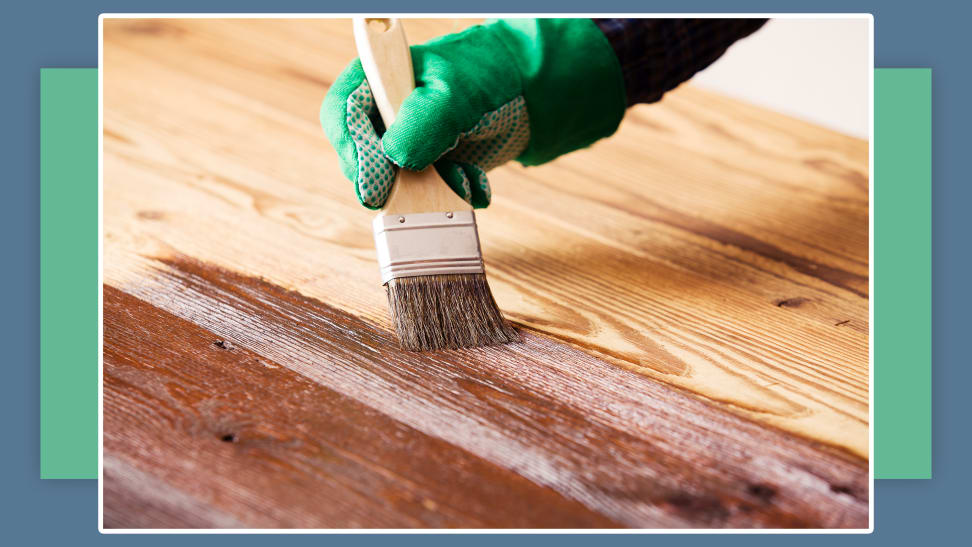 A hand holding a paint brush to stain a deck