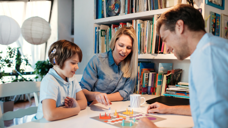 Family of three playing board game together indoors.