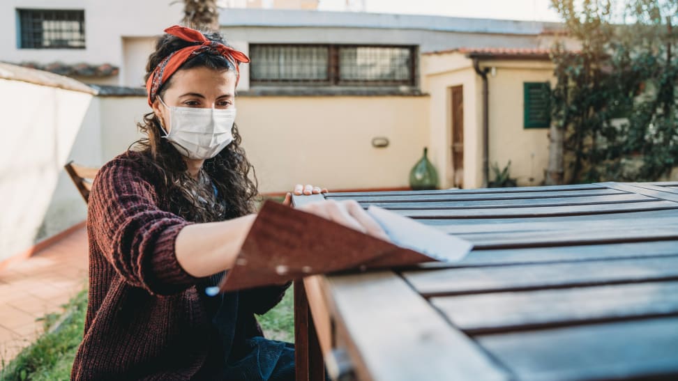 A person sands a wooden table in the backyard of their home.