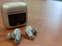 The JBL Tour Pro 2 earbuds sitting in front of their case on a wooden table.