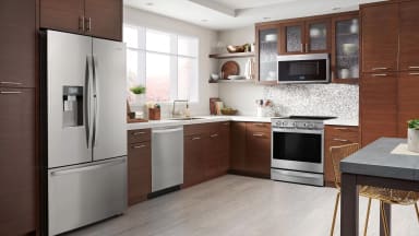 Modern kitchen with stainless steel refrigerator, dishwasher, oven, and microwave set among dark wood cabinets.