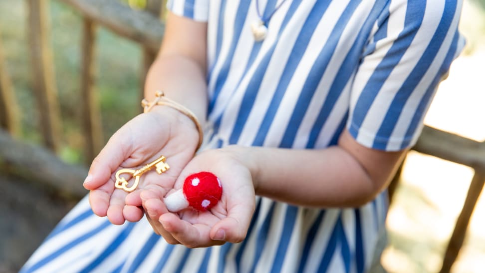 A pair of cupped hands holding a small felt mushroom and a small gold key