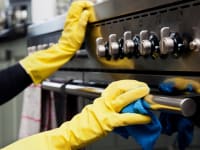 A person wipes a stainless steel oven with a microfiber towel.
