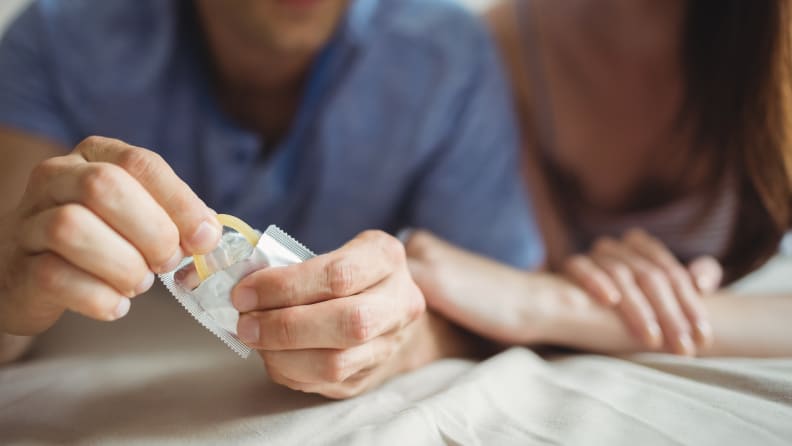 A couple opening a condom.