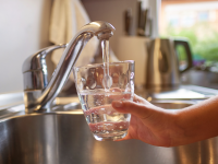 Close-up of arm holding a cup under running faucet