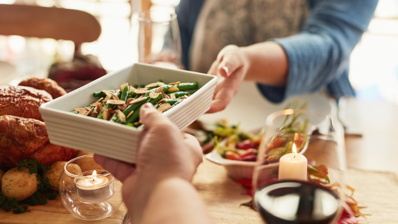 Two people passing a casserole dish of green beans between them.