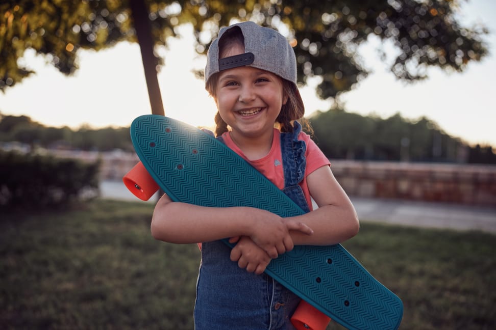 A girl smiles as she hugs her Penny Board beginner skateboard for kids.