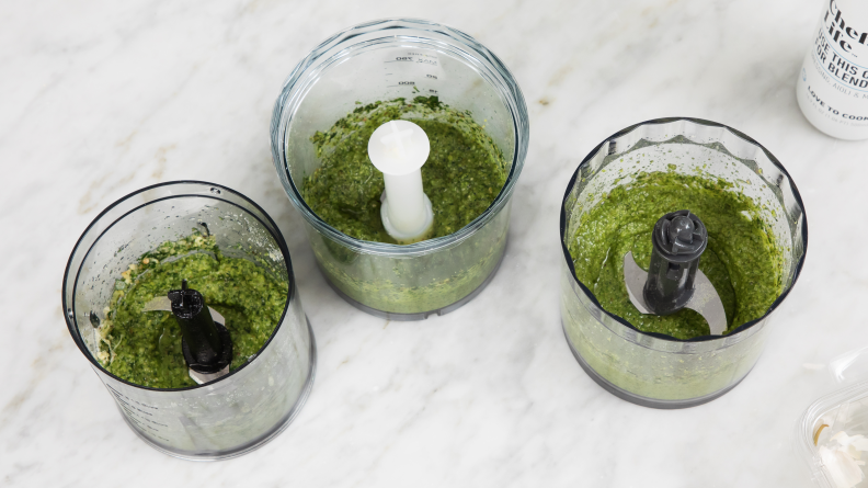 Three food processors full of pesto on a marble surface