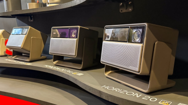 Three XGIMI Horizon 20 series projectors are displayed side by side on a curved shelf, labeled as Horizon 20, Horizon 20 Pro, and Horizon 20 Max. Each projector has a rectangular design with a front-facing speaker grille and lens, set in a matte finish casing.