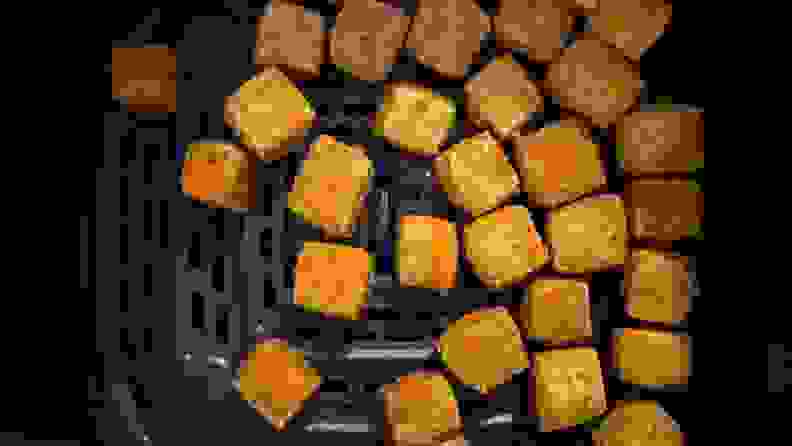 Cubes of air fried tofu sitting in the bottom of an air fryer.