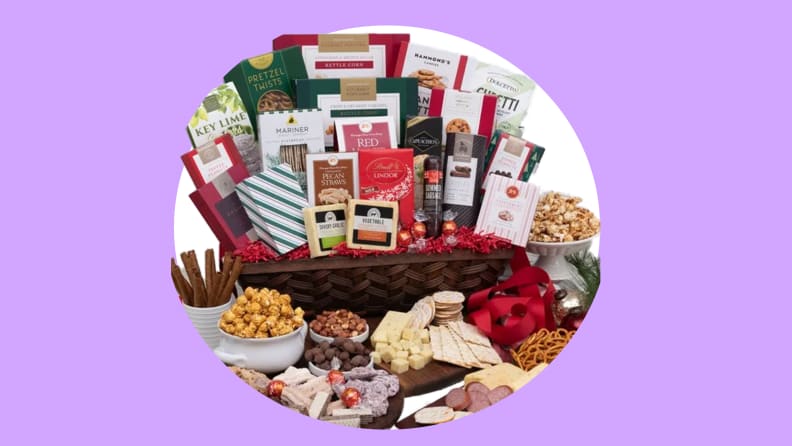 An assortment of chocolates, pretzels, pocorn, and cheeses in and in front of a brown wicker hamper.