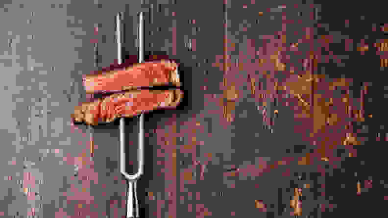 A BBQ fork holding two slices of medium rare steak