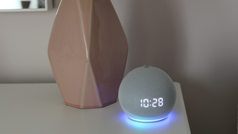 An Amazon Echo Dot sits on a nightstand next to a bedside lamp.