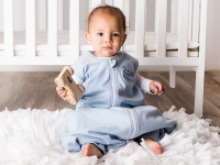 婴儿床前坐着一个婴儿，他穿着一个蓝色的魔法梅林魔法梦袋。