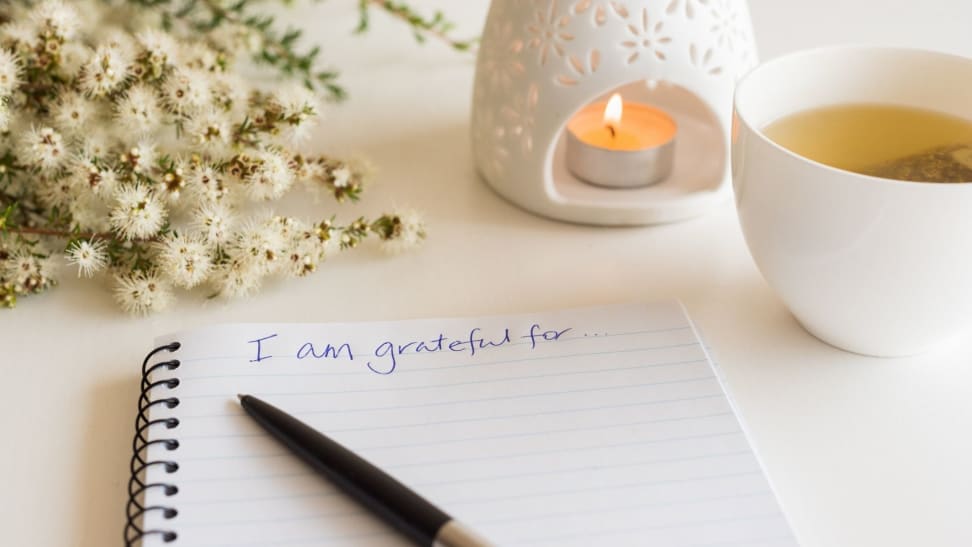 a gratitude journal open on table next to tea and a candle