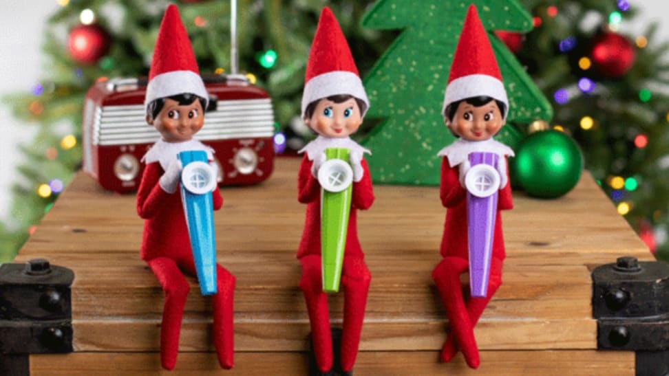 A row of three elves sitting on a shelf playing kazoos.
