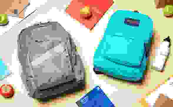 An L.L. Bean backpack and JanSport backpack laying on a table surrounded by school supplies and apples.