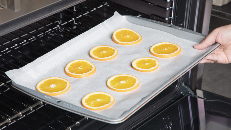A person reaching into the oven with a tray of orange slices.