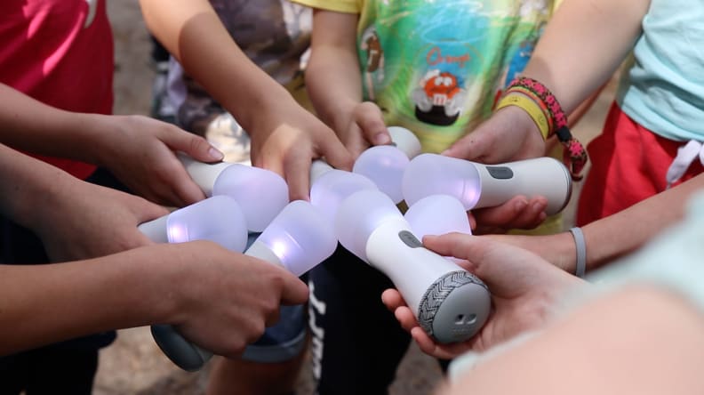 A group of kids hands reach into a circle, all holding glowing electronic wands from the Picoo toy set.