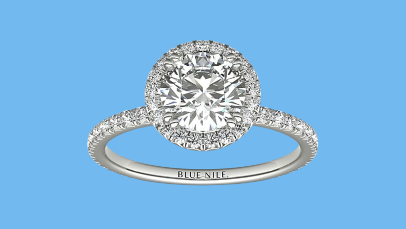 An image of a halo diamond ring in platinum with diamonds surrounding a large round central diamond, and additional diamonds studding the band.