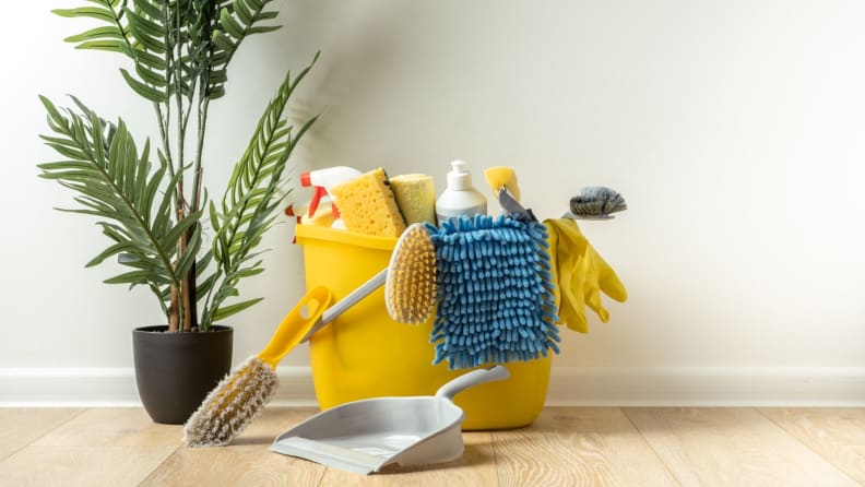 A yellow bucket of cleaning supplies to the right of a houseplant.