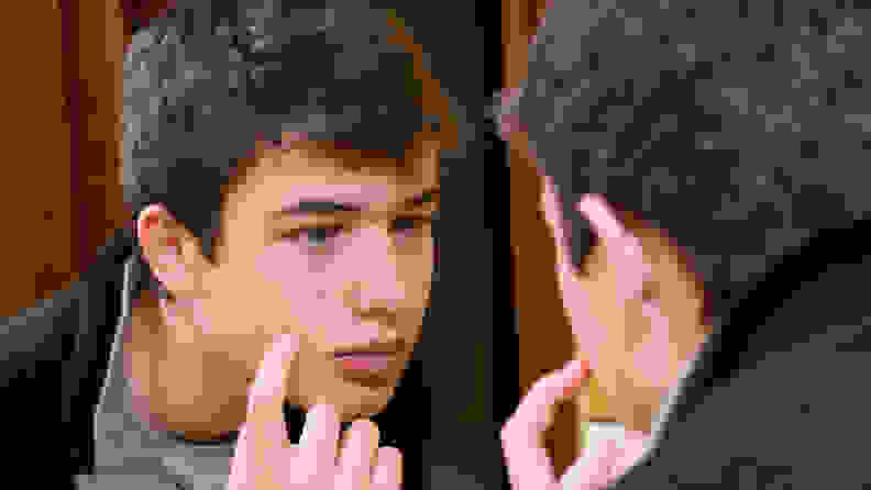 A young man looking into a mirror and touching his face.
