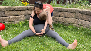 A pregnant woman sitting on the grass holding her bump and hugging an older child