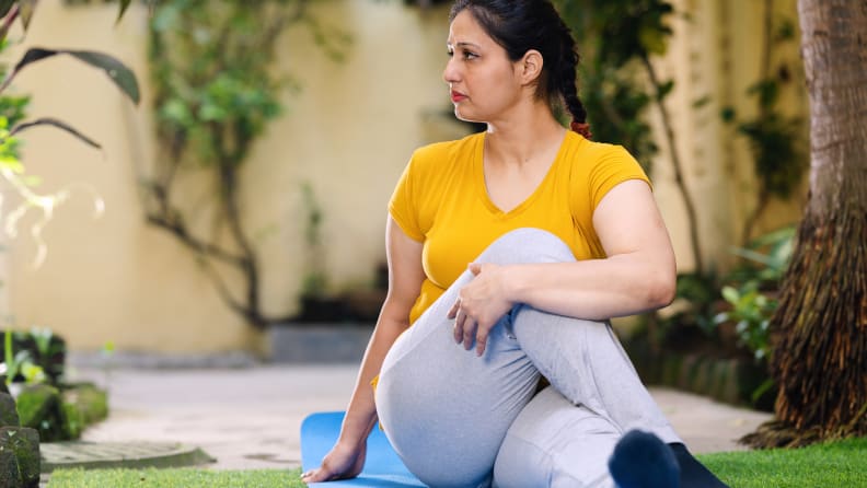 Outdoor image of Asian/ Indian woman doing morning exercise and yoga in garden on exercise mat. She is stretching her body which help ease back pain, flexible body and relief in mussels.