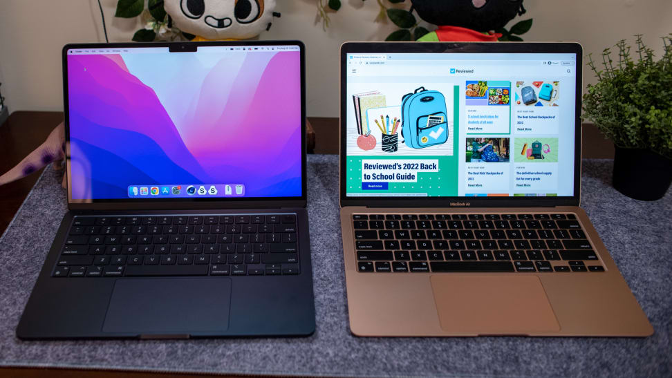 Black MacBook Air and rose gold MacBook Air 15 laptops side by side on top of blue cloth in front of plush stuffed animals and potted plant.