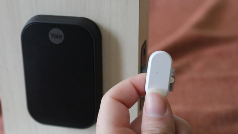 A hand holding the smart lock's oval sensor up to the smart lock itself.