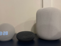 Amazon Echo, Google Home, and Apple HomeKit smart speakers all sit next to each other on a blue table.