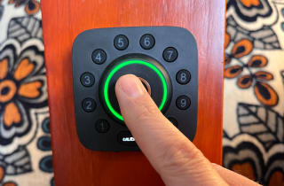 A person's finger pressing buttons on a smart door lock