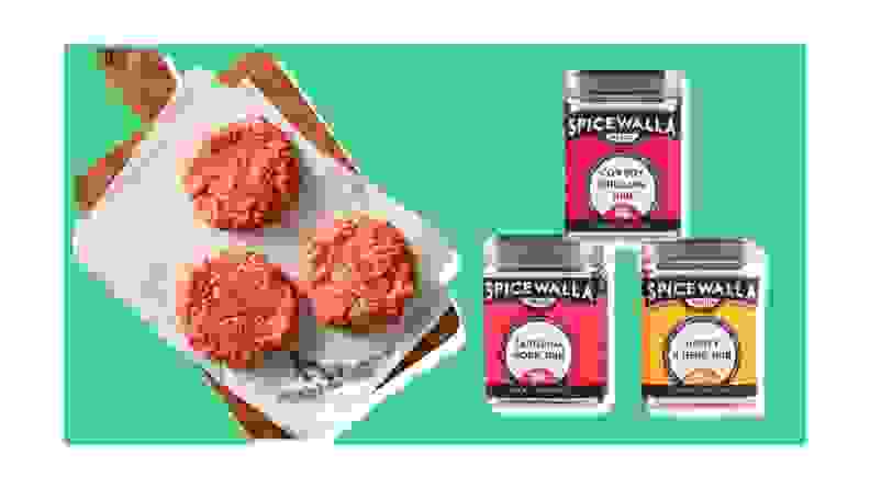 Raw burger patties on a tray, next to three containers of spices on a green background.