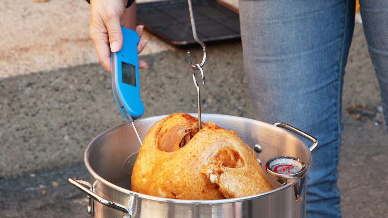 A person using a digital meat thermometer to measure a fried turkey temperature.