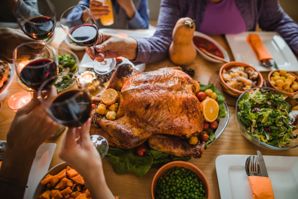 A group of people toasting with glasses of red wine over  a roast turkey.