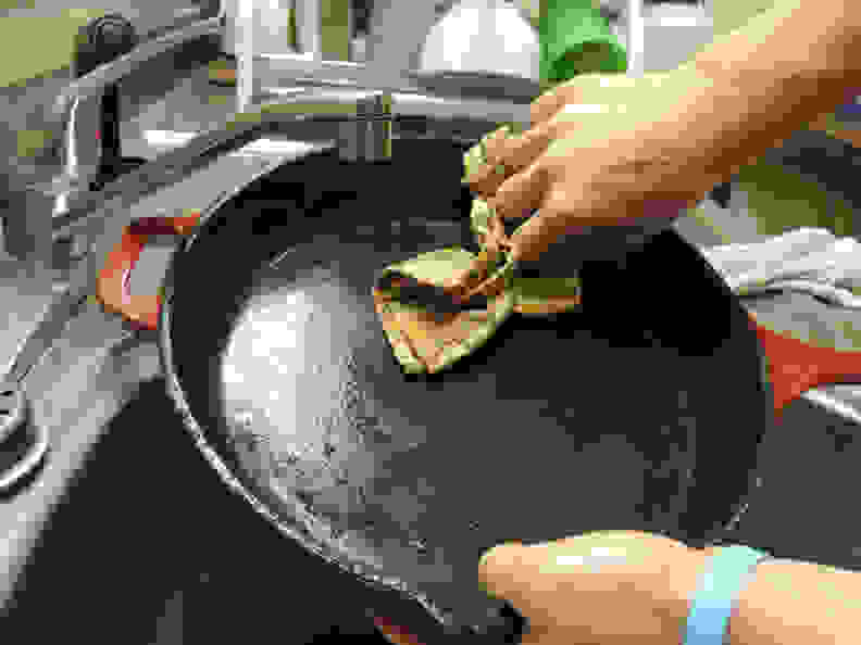 A person wipes a cast-iron pan with a cloth.