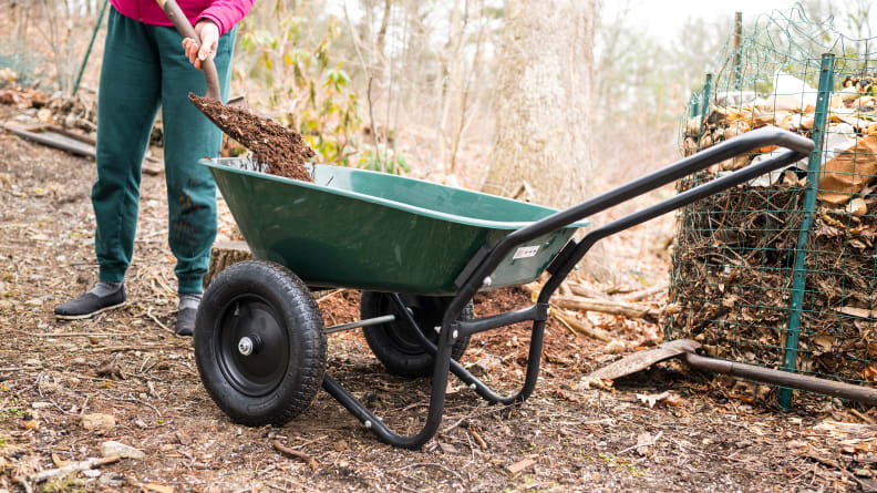 A person uses a shovel to fill the Marathon Green Yard Rover with dirt.