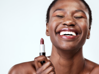 Woman smiling while holding a tube of brown nude lipstick