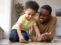 A father and young son complete a puzzle together on the floor.