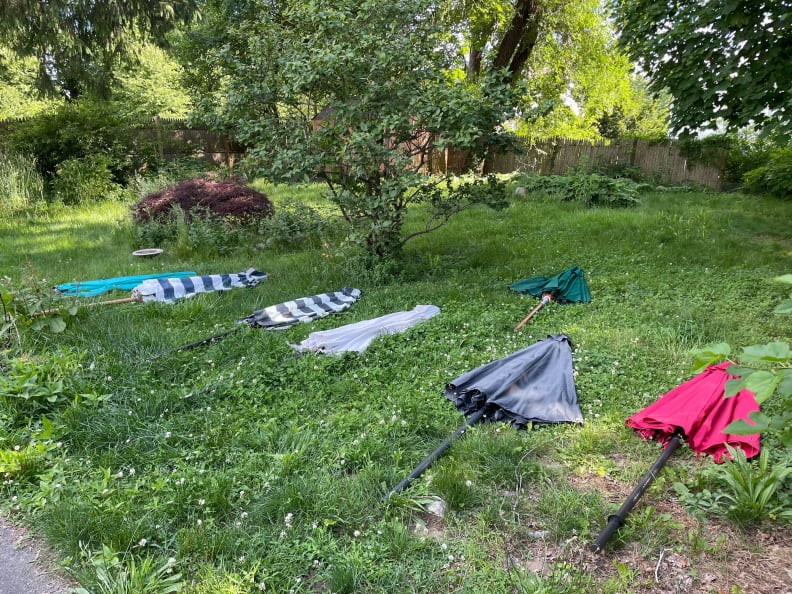 Folded up patio umbrellas lay flat on the green grass.