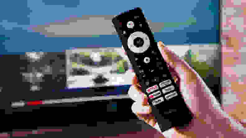 A person holds a remote control to a television set.