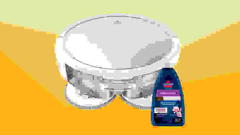 A white Bissell robot vacuum with a bottle of Bissell floor cleaner against a varied yellow background.