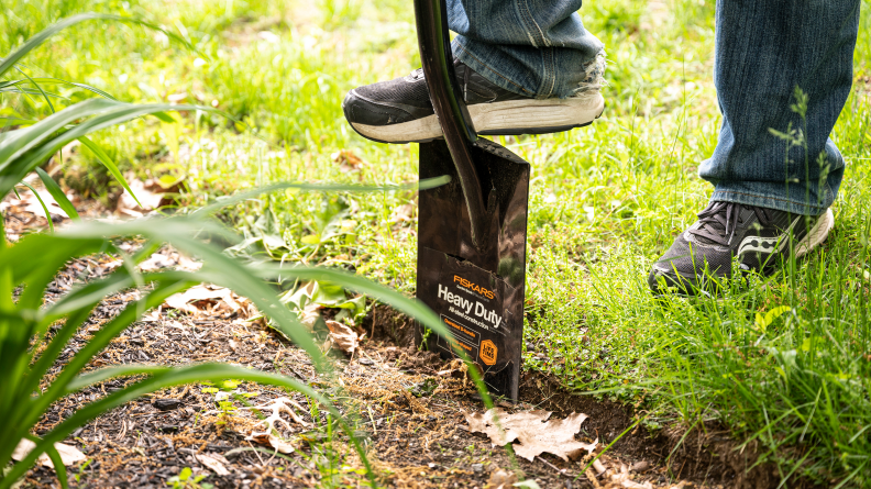 A person pushing a spade shovel into the ground using their foot