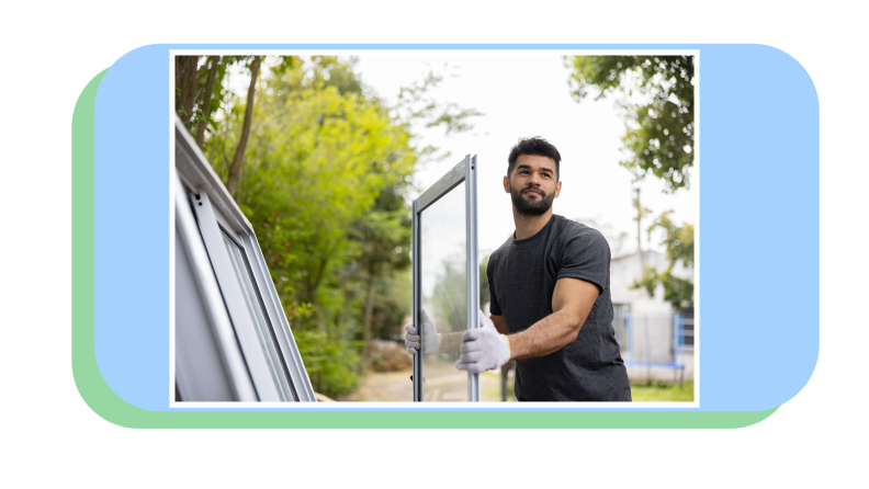 Person wearing gloves carrying new window and frame to install on home.