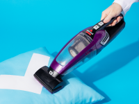 Demonstrating the purple Bissell Pet Hair Eraser 2390 vacuum on a pillow (which features our Reviewed checkmark logo).