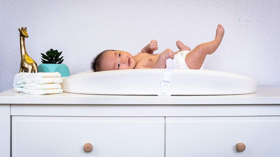 Baby laying down on changing table on top of dresser.