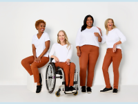 Four women, with one sitting in a wheelchair, are all wearing white T-shirts and Adaptive Denim Co. orange jeans.