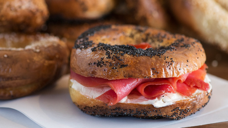 A Montreal-style bagel, stuffed with smoked salmon and cream cheese. More Montreal-style bagels are in the background.