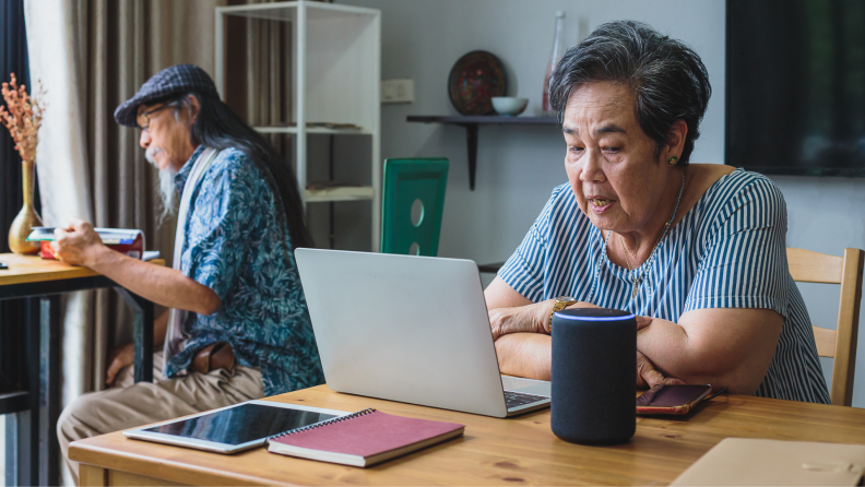 A person sits at a desk using a laptop and smart speaker.